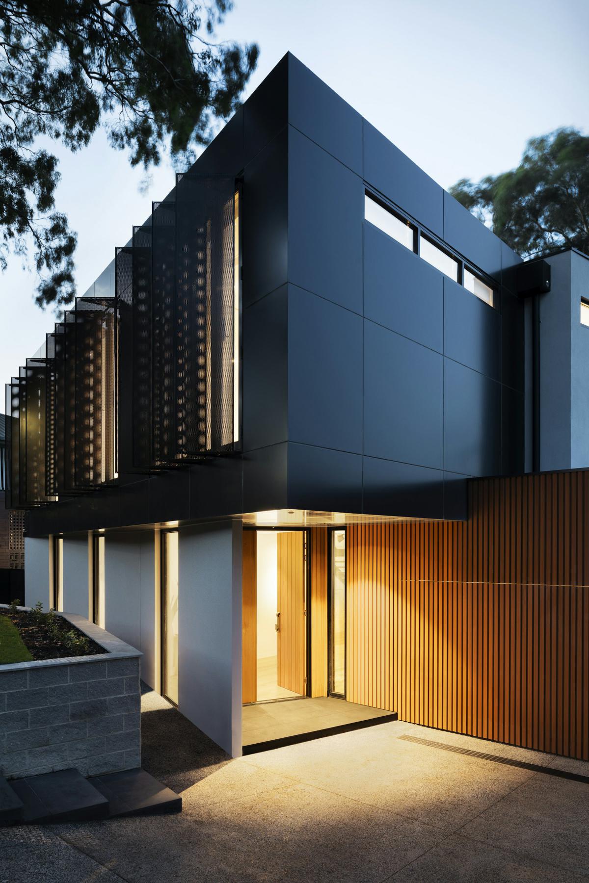 Dark contemporary facade with vertical timber screens and warm lighting
