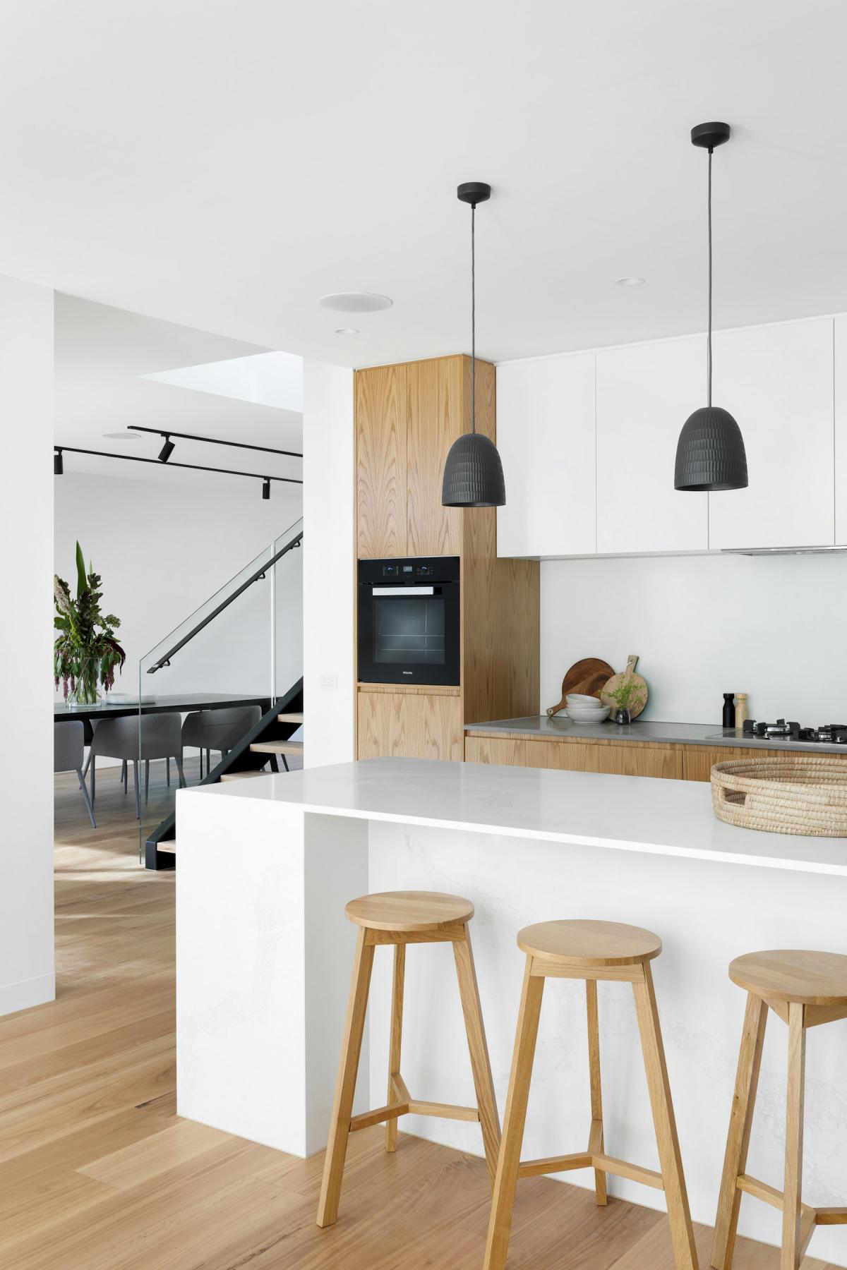 Handleless modular kitchen with timber tall units and white counters Handleless modular kitchen with timber tall units and white counters